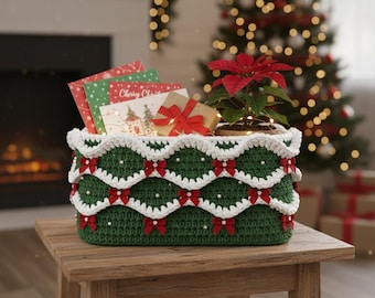 May include: A green crochet basket with white scalloped edging, red bows, and pearl detailing. The basket contains Christmas cards, a small wrapped gift, and a poinsettia plant. It sits on a wooden table, with a Christmas tree visible in the background.