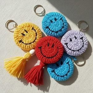 May include: A selection of handmade crochet smiley face keyrings in yellow, blue, red, purple, and light blue. Each keyring has a black embroidered smile and a metal ring. Some keyrings have matching tassels.
