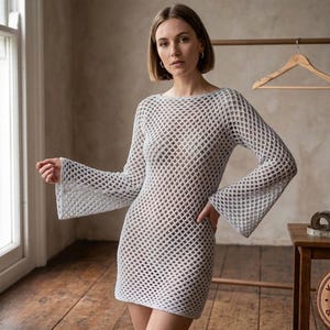 May include: A light gray, open-weave dress with long sleeves and flared cuffs. The dress has a scoop neckline and a fitted silhouette. The fabric appears to be a crochet or knit design. The dress is knee-length.