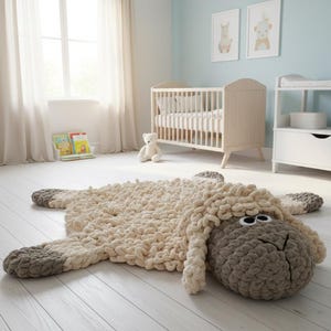 May include: A cream-colored, sheep-shaped rug with gray accents. The rug is made of a chunky, looped yarn and features a detailed sheep face with large black eyes. The rug is placed on a white wooden floor in a nursery setting.