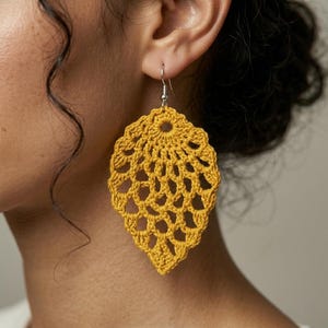 Op de afbeelding: Mosterdgele gehaakte blad oorbellen met een zilveren haak. De oorbellen hebben een open, kantachtig ontwerp en een druppelvorm. De oorbellen zijn een handgemaakt accessoire.