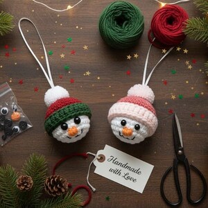 May include: Two handmade crochet snowman ornaments with red, green, and white hats, and black button eyes. The scene includes yarn, scissors, a mug of cocoa, and a tag that says "Handmade with Love."
