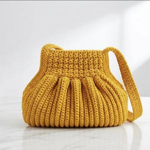 May include: A mustard yellow crochet handbag featuring a structured top opening and a pleated, ribbed body texture. The bag includes a single integrated shoulder strap and is crafted from thick yarn with a consistent, dense stitch pattern throughout.