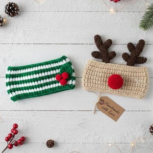 May include: Two handmade crochet headbands. One is green and white striped with a holly berry accent. The other is tan with brown antlers and a red pom-pom nose. A tag reads "Handmade with Love".