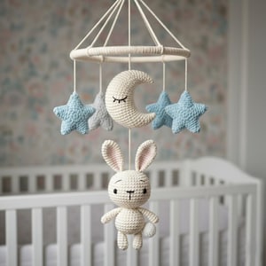 Könnte beinhalten: Handgefertigtes Baby-Mobile aus Häkelarbeit mit einem weißen Hasen, einem Halbmond und blauen und grauen Sternen. Das Mobile ist an einem kreisförmigen Rahmen mit weißer Schnur aufgehängt und für die Anbringung über einem Kinderbett konzipiert.