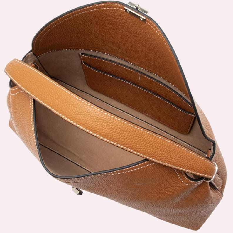 May include: A tan leather handbag with a top handle and a silver clasp. The bag has white stitching and a textured exterior. The interior features pockets and a light brown lining. The bag is open, revealing the inside.