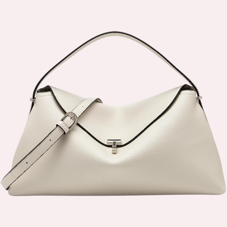 May include: A white leather handbag with a top handle and a detachable shoulder strap. The bag features a flap closure with a silver-tone clasp and black trim. The bag has a textured surface.
