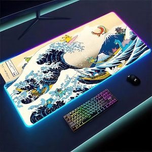 Puede incluir: Alfombrilla de ratón rectangular para juegos con un diseño inspirado en "La Gran Ola de Kanagawa" de Hokusai, con personajes de dibujos animados surfeando la ola. La alfombrilla tiene un borde azul brillante, un teclado y un ratón.