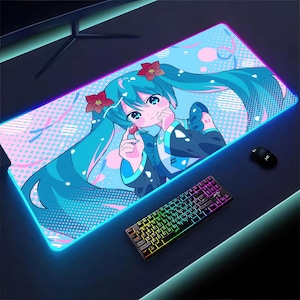 Könnte beinhalten: Rechteckiges Gaming-Mauspad mit einer lebendigen Anime-Illustration eines Charakters mit langen türkisfarbenen Haaren und roten Blumen-Haarschmuck. Das Mauspad hat einen leuchtenden blauen Rand, eine schwarze Maus und eine farbenfrohe Tastatur.