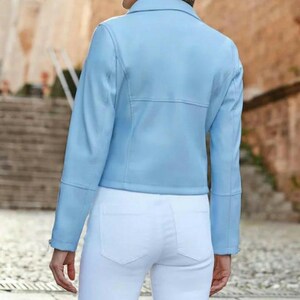 May include: A light blue jacket with long sleeves and a collared neckline. The jacket has a tailored fit and is paired with white pants. The image is taken from the back, showcasing the jacket's design and the overall outfit.