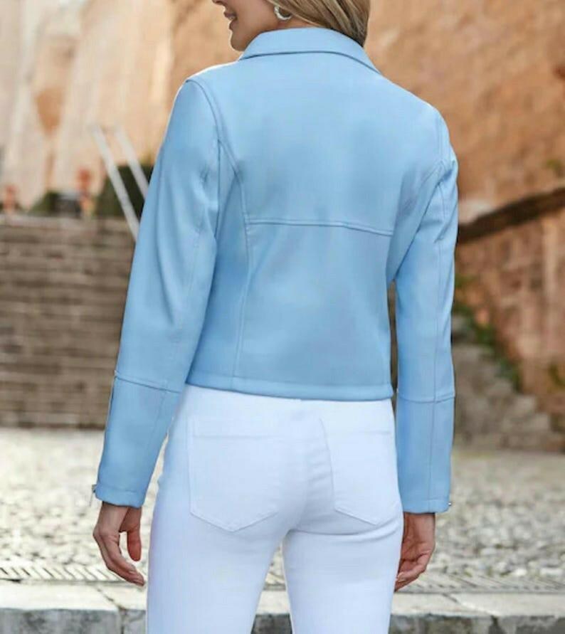 May include: A light blue jacket with long sleeves and a collared neckline. The jacket has a tailored fit and is paired with white pants. The image is taken from the back, showcasing the jacket's design and the overall outfit.