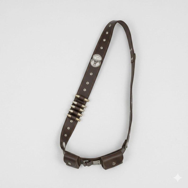 May include: A dark brown leather bandolier strap featuring a series of metal eyelets, a silver-toned circular emblem, and five metallic bullet casings held in place. The strap includes two small rectangular pouches attached at the lower section.