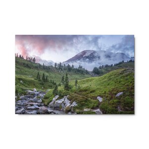 May include: A misty mountain landscape with a stream flowing through a valley. The sky is a soft pink and purple, and the mountain peaks are covered in clouds.