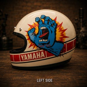Peut inclure: Un casque de moto crème arborant un graphique bleu représentant une main hurlante sortant d'une étoile rouge et jaune. Le casque présente une bande horizontale rouge avec le texte blanc YAMAHA et une bordure noire sur le bas.