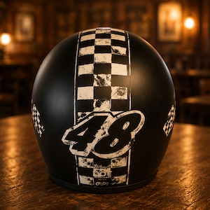 May include: A matte black motorcycle helmet featuring a vertical white checkered racing stripe down the centre. The number 48 is printed in a large, distressed white font over the stripe. Smaller checkered flag patterns appear on the sides.