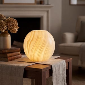 May include: A spherical lamp made of translucent, cream-colored stone with visible natural veining. The lamp emits a warm, soft glow, highlighting the organic, layered patterns within the stone material. It is a round, smooth lighting fixture.