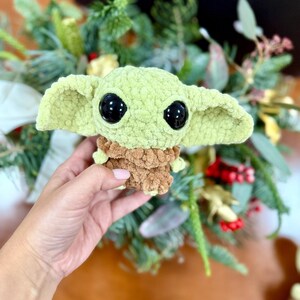 May include: A light green crocheted doll with large black eyes and oversized ears. The doll has a brown textured body and is approximately 4 inches tall. The doll is a character from a popular science fiction franchise.