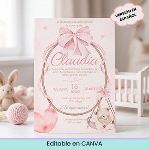 Puede incluir: Una tarjeta de invitación rectangular para baby shower en rosa suave con un gran lazo de acuarela en la parte superior, un marco ovalado central y un osito de peluche en un columpio. El texto incluye el nombre Claudia, fecha y lugar.