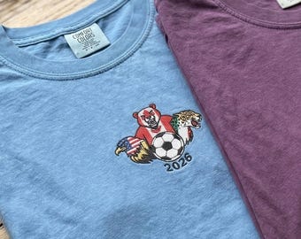 Camiseta bordada con las mascotas del Mundial 2026: Camiseta cómoda con banderas de países y diseño de balón de fútbol.