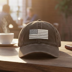 May include: A brown baseball cap with an embroidered American flag patch. The cap is made of a soft, worn material and has a curved brim. The flag features a detailed design with stars and stripes.