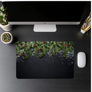 May include: A black rectangular mousepad featuring a festive Christmas design. The top of the mousepad displays green pine branches with red berries and a dusting of white snow. A white computer mouse is on the right.