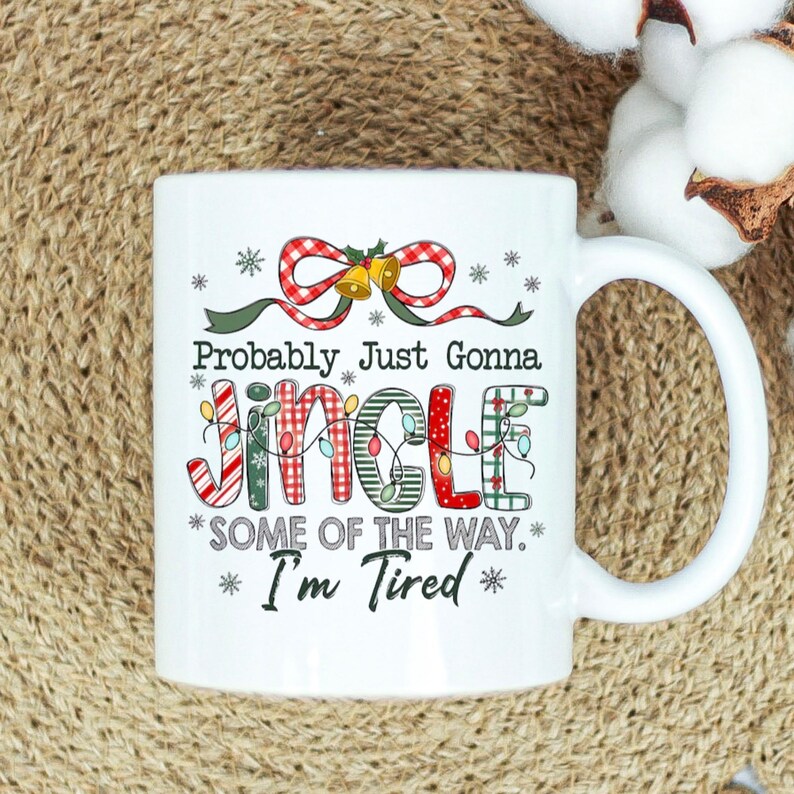 May include: White ceramic mug with a Christmas-themed design. The mug features the text "Probably Just Gonna Jingle *SOME OF THE WAY.* *I'm Tired*" in a festive font with red, green, and white accents. A red bow and bells are at the top.