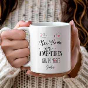 May include: White ceramic mug with the text "New Home, New Adventures, New Memories" in black script. The mug features a moving truck graphic and a house graphic with a heart. The name "Smith's" is printed at the bottom.