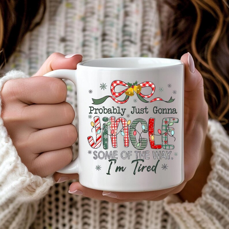 May include: White ceramic mug with the text "Probably Just Gonna Jingle *SOME OF THE WAY.* I'm Tired *" in a festive Christmas design. The mug features a red and white plaid bow with bells and snowflakes.