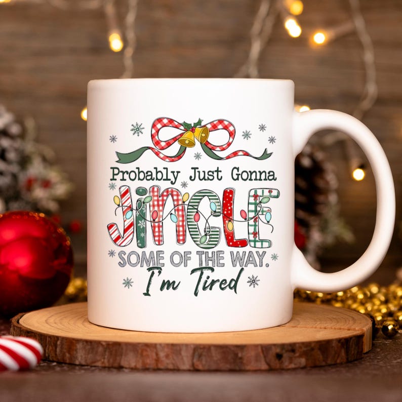 May include: White ceramic mug with a Christmas-themed design. The mug features the text "Probably Just Gonna Jingle Some of the Way. I'm Tired" in festive colors and fonts, with decorative snowflakes and a bow.