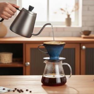 Pode incluir: Uma chaleira de pescoço de ganso de aço inoxidável despeja água quente sobre um coador de café de cerâmica azul. O coador está sobre uma jarra de vidro cheia de café. Grãos de café espalhados sobre a mesa de madeira.