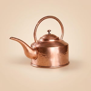 May include: A copper kettle with a hammered finish. The kettle has a curved spout, a rounded body, and a large arched handle. The lid is topped with a small knob. The kettle is a warm, reddish-brown color.