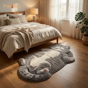 May include: A plush, grey and white area rug shaped like a sleeping cat with its belly facing upward. The rug features a soft, textured surface with detailed paw pads and a peaceful facial expression, lying flat on a wooden floor in a bedroom setting.