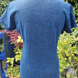 May include: A short-sleeved t-shirt in a dark blue acid-wash finish. The garment features a round neckline with a ribbed trim and matching ribbed detailing on the sleeve cuffs. The fabric has a mottled, textured appearance throughout the surface.