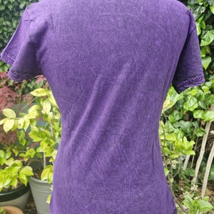 May include: A short-sleeved t-shirt in a deep purple color with a mottled, acid-wash texture. The garment features a crew neckline and visible stitching along the sleeve hems and bottom hem, displaying a consistent dark purple hue throughout.