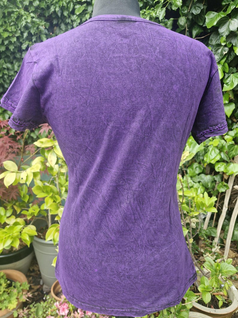 May include: A short-sleeved t-shirt in a deep purple color with a mottled, acid-wash texture. The garment features a crew neckline and visible stitching along the sleeve hems and bottom hem, displaying a consistent dark purple hue throughout.