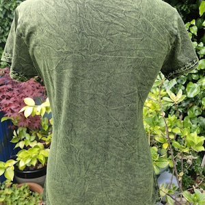 May include: A short-sleeved t-shirt in a dark olive green acid wash finish. The garment features a crew neckline and visible light green decorative stitching along the sleeve cuffs, providing a textured appearance throughout the fabric surface.