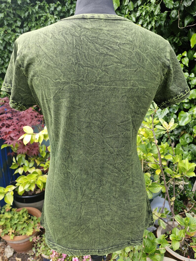 May include: A short-sleeved t-shirt in a dark olive green acid wash finish. The garment features a crew neckline and visible light green decorative stitching along the sleeve cuffs, providing a textured appearance throughout the fabric surface.
