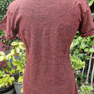 May include: A short-sleeved t-shirt featuring a dark red and black acid-wash pattern. The garment has a round neckline and visible stitching along the sleeve hems. The fabric displays a mottled, textured appearance throughout the entire surface.