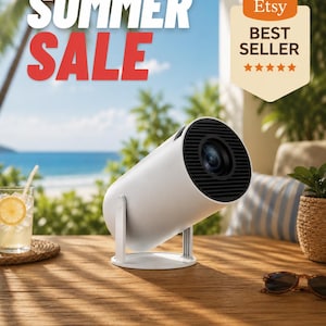 Op de afbeelding: Een witte cilindrische projector met een zwarte lens en rooster staat op een houten tafel. De woorden "SUMMER SALE" staan in grote witte en rode letters. Een "Etsy Best Seller"-badge is zichtbaar. Een glas limonade en een zonnebril staan ook op de tafel.