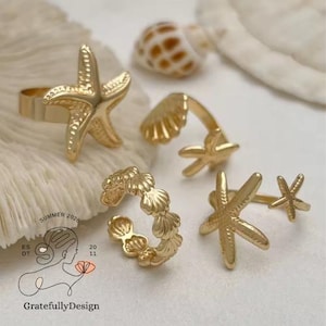 Könnte beinhalten: Goldfarbene Ringe mit Muschel- und Seestern-Designs. Die Ringe umfassen einen Seesternring, einen Muschelring und einen Ring mit einem Seestern und einem kleineren Seestern. Das Bild enthält auch eine Muschel und den Text "Summer 2026" und "GratefullyDesign".
