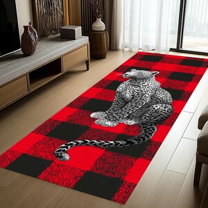 May include: A rectangular area rug featuring a red and black buffalo plaid pattern. A detailed illustration of a leopard in shades of gray and white is centered on the rug. The leopard is in a seated position with its tail extending.