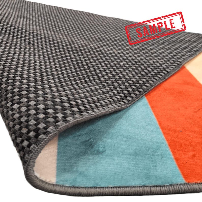 Puede incluir: Una secci&oacute;n de una alfombra colorida con un dise&ntilde;o geom&eacute;trico. La alfombra presenta un respaldo gris a cuadros, una secci&oacute;n azul turquesa, una secci&oacute;n naranja y una secci&oacute;n color crema. La palabra "SAMPLE" est&aacute; estampada en la alfombra.