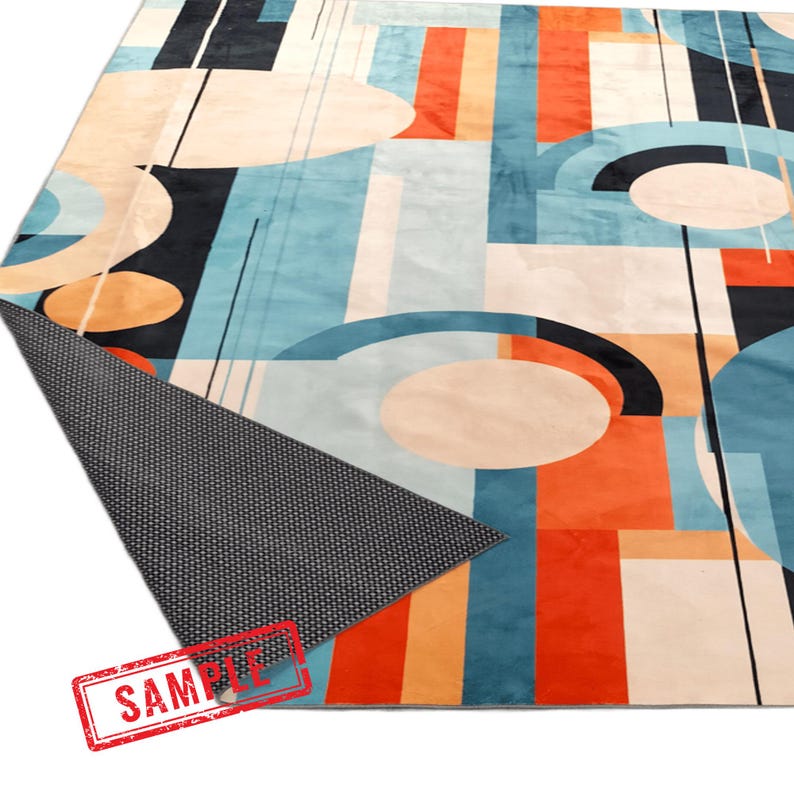 May include: A large, rectangular area rug with a geometric design. The rug features a mix of colors, including blue, orange, black, and cream. The pattern consists of abstract shapes and lines. The rug's underside is visible, showing a dark gray, textured backing.