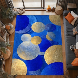 Op de afbeelding: Een blauw rechthoekig vloerkleed met een patroon van overlappende cirkels in goud, zilver en blauw. Het vloerkleed heeft een textuur, wat visuele interesse toevoegt aan de vloerbedekking.