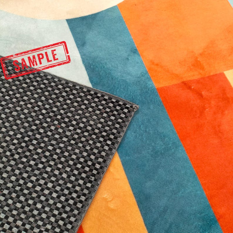 May include: A colorful rug sample with a geometric design. The rug features a checkerboard pattern in gray and black, alongside sections of blue, orange, and cream colors. The word "SAMPLE" is stamped in red.