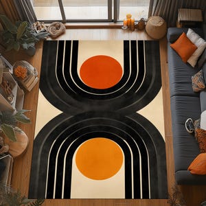 May include: A large, rectangular area rug with a modern geometric design. The rug features a cream-colored background with two large black arch shapes, each containing a bright orange circle. The rug is a statement piece for any living space.