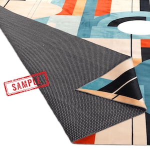 May include: A modern area rug with a geometric design featuring shapes in teal, orange, black, and beige. The rug's underside is a dark gray, textured material. The word "SAMPLE" is stamped in red on the rug.