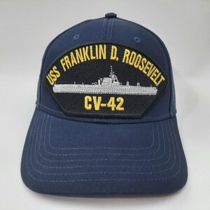 May include: Navy blue baseball cap featuring a patch with the text "USS FRANKLIN D. ROOSEVELT" and "CV-42". The patch also includes a detailed illustration of a ship. The cap has a curved brim and a structured crown.