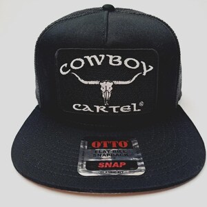 May include: Black flat-bill snapback hat with a mesh back. The hat features a rectangular patch with the words "COWBOY CARTEL" in white, along with a steer skull graphic. The hat has a "OTTO" tag.