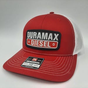 May include: Red and white trucker hat with the text "DURAMAX DIESEL" on a black and white patch. The hat has a red brim and crown with a white mesh back. The Richardson brand tag is visible.